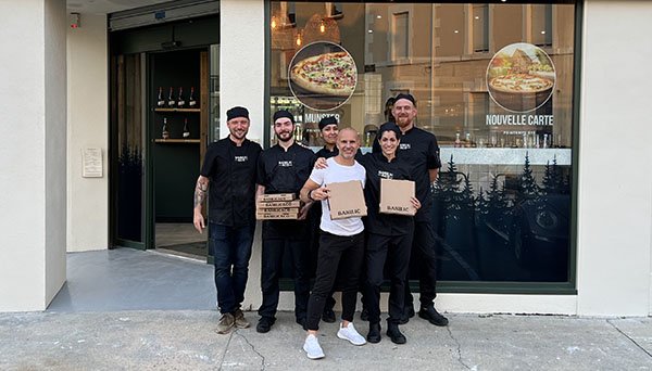 Tatiana Schmitt franchisée de Basilic & Co Périgueux, entourée de son équipe et de l'un des formateurs de l'enseigne. Tous sourient et tiennent des boites à pizzas devant le restaurant.